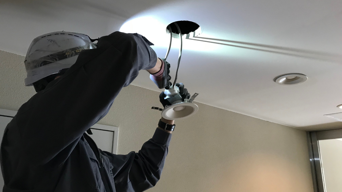 Person installing a light fixture in a ceiling, wires exposed.