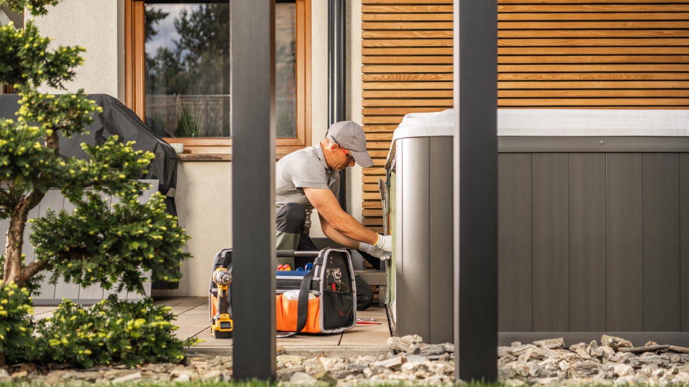 Man in gray cap working on a hot tub in an outdoor setting; tools visible.