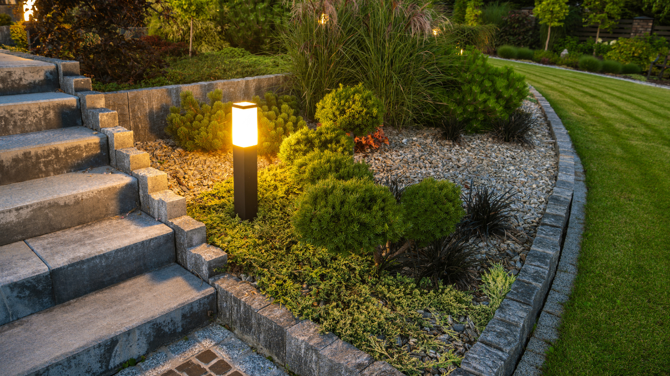 Illuminated garden bed with stone steps, gravel, and lawn, featuring a glowing lamp.