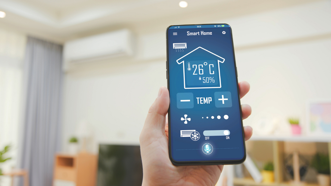 Hand holding a smartphone displaying a smart home app to control AC unit in a modern living room.