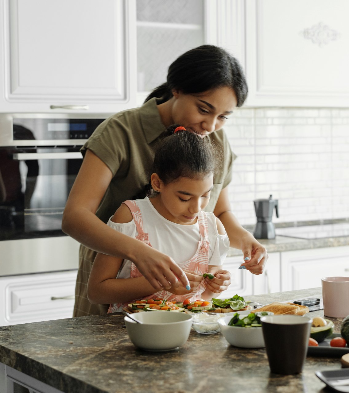 mother helping young daughter prepare food in kitchen