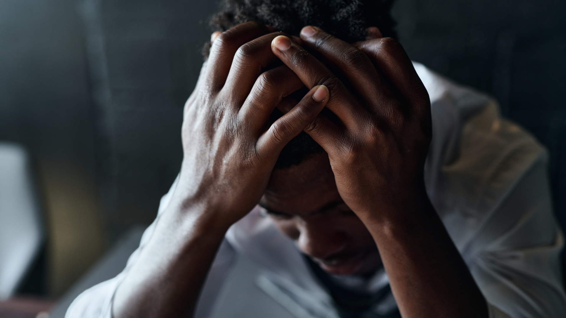 A person in a white shirt with their head in their hands, expressing distress or deep concern.