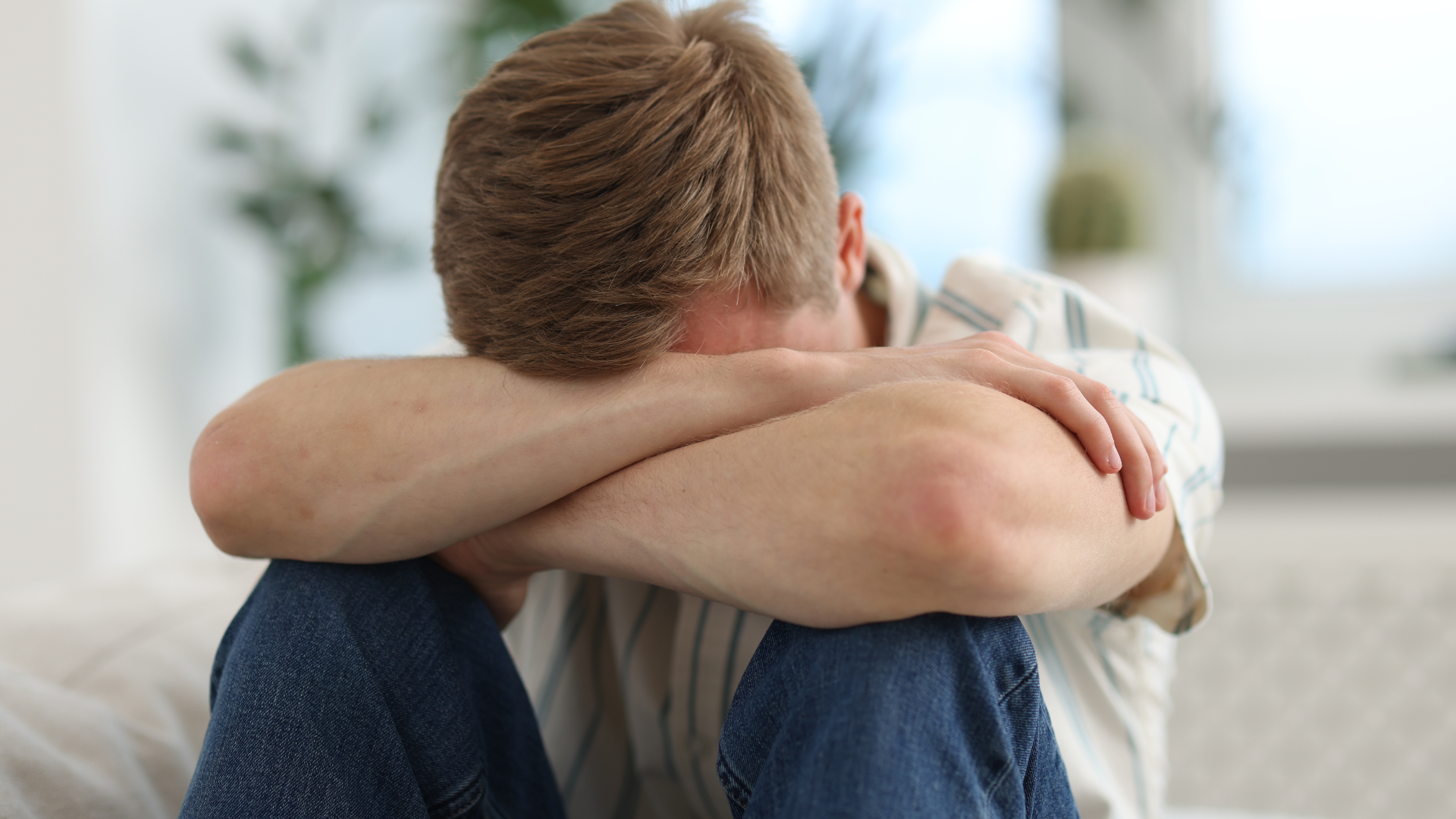 A person sits slumped over with their head resting on their crossed arms in a position of distress or sadness.