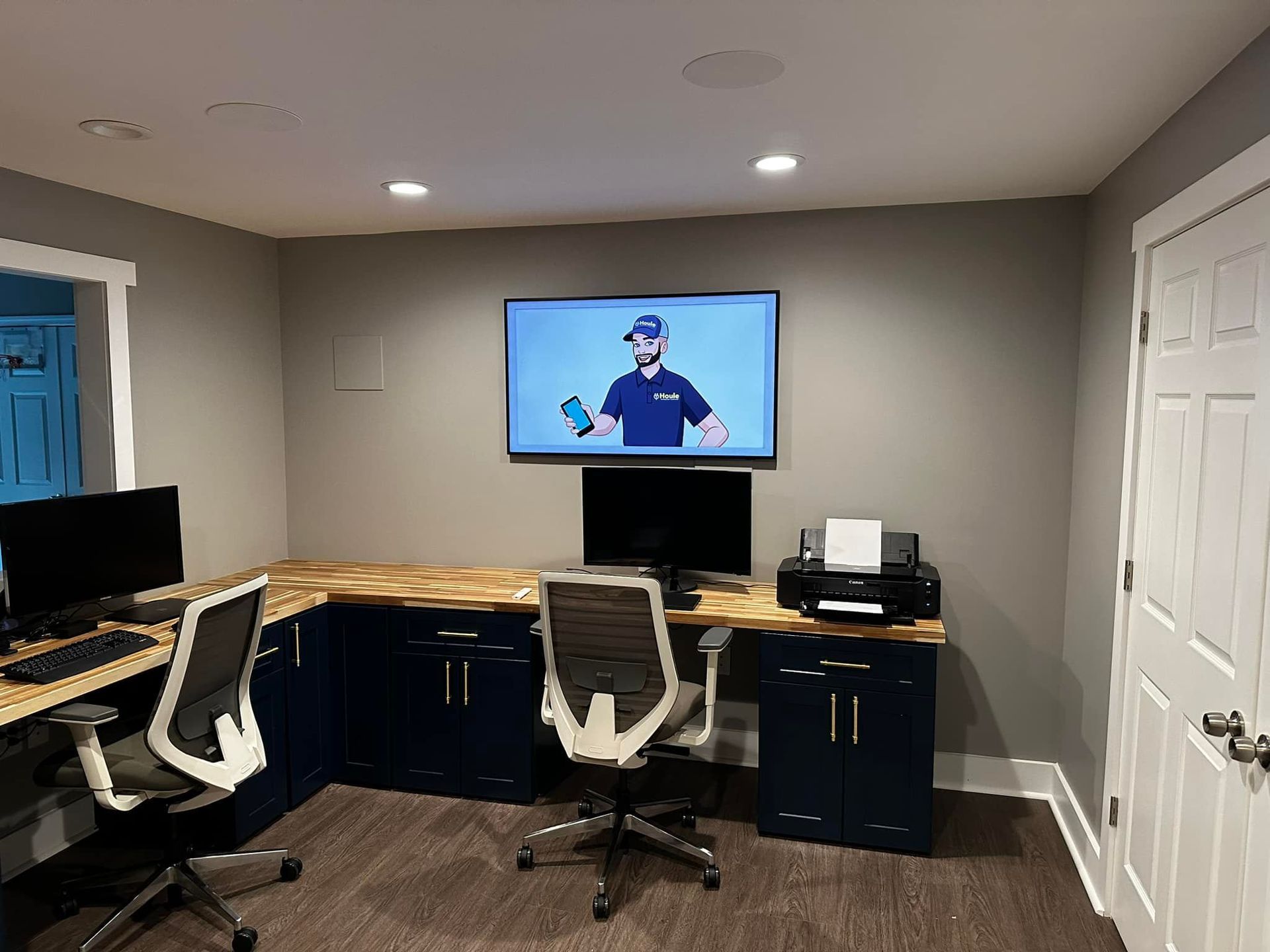 a home office with two desks , two chairs , a printer and a newly installed flat screen tv .