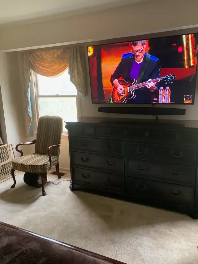 a man is playing a guitar on a newly installed television in a living room with the floating soundbar