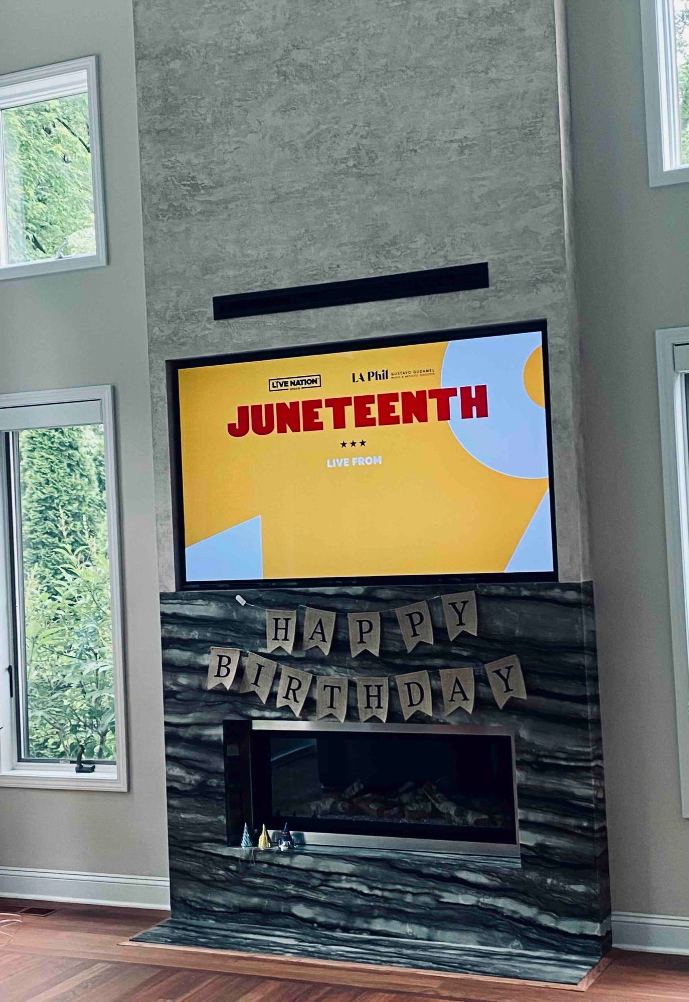 a living room with a birthday decoration on a fireplace and a newly installed flat screen tv on the wall .