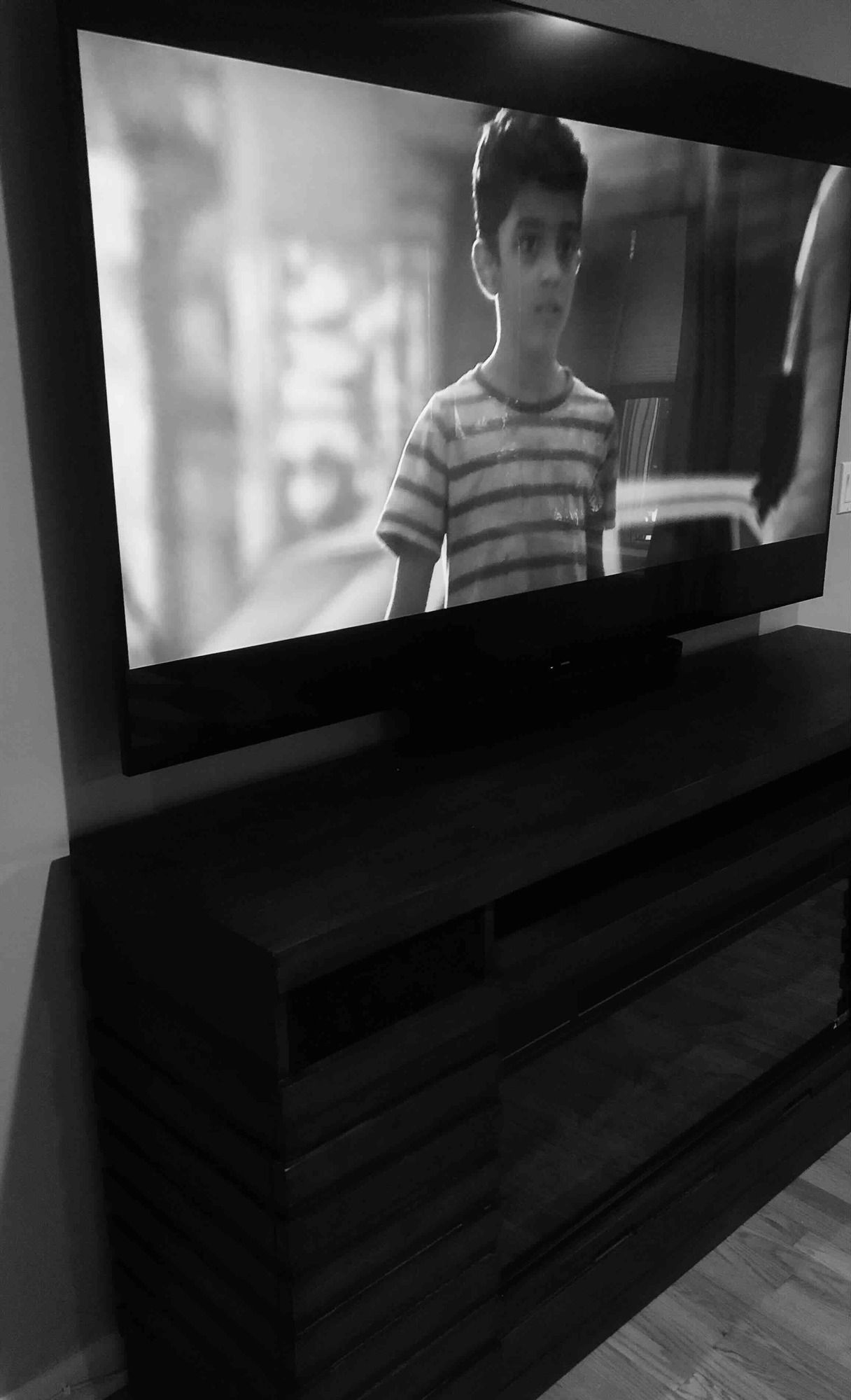 a black and white photo of a boy watching a movie on a newly installed television .
