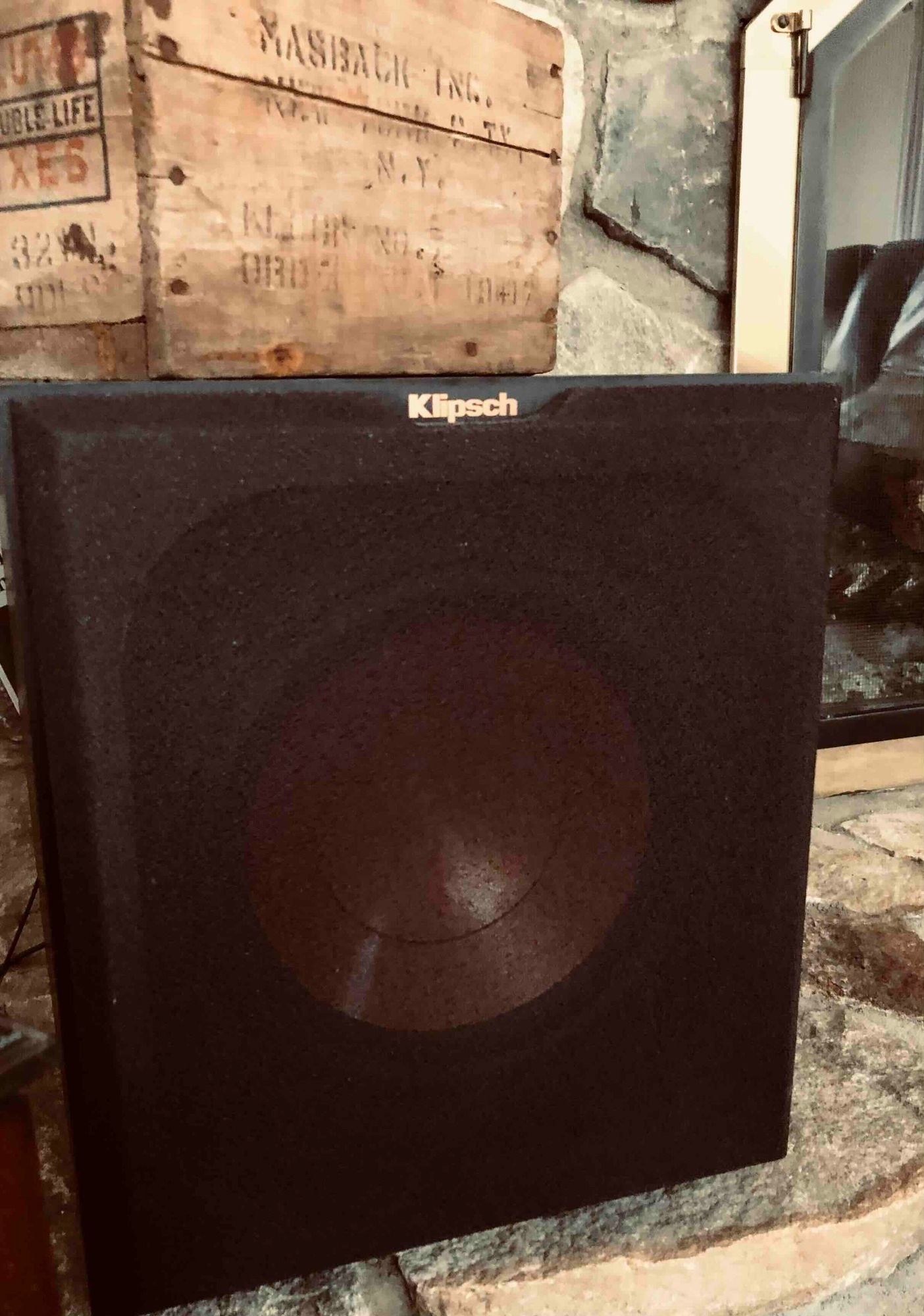 a black subwoofer is sitting on top of a stone fireplace next to a wooden box .