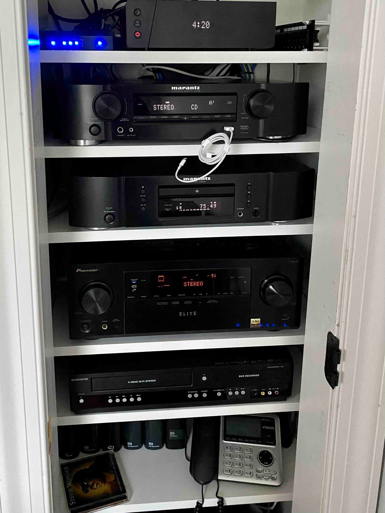 a closet filled with a variety of electronic devices including a dvd player and a phone for the multi audio room