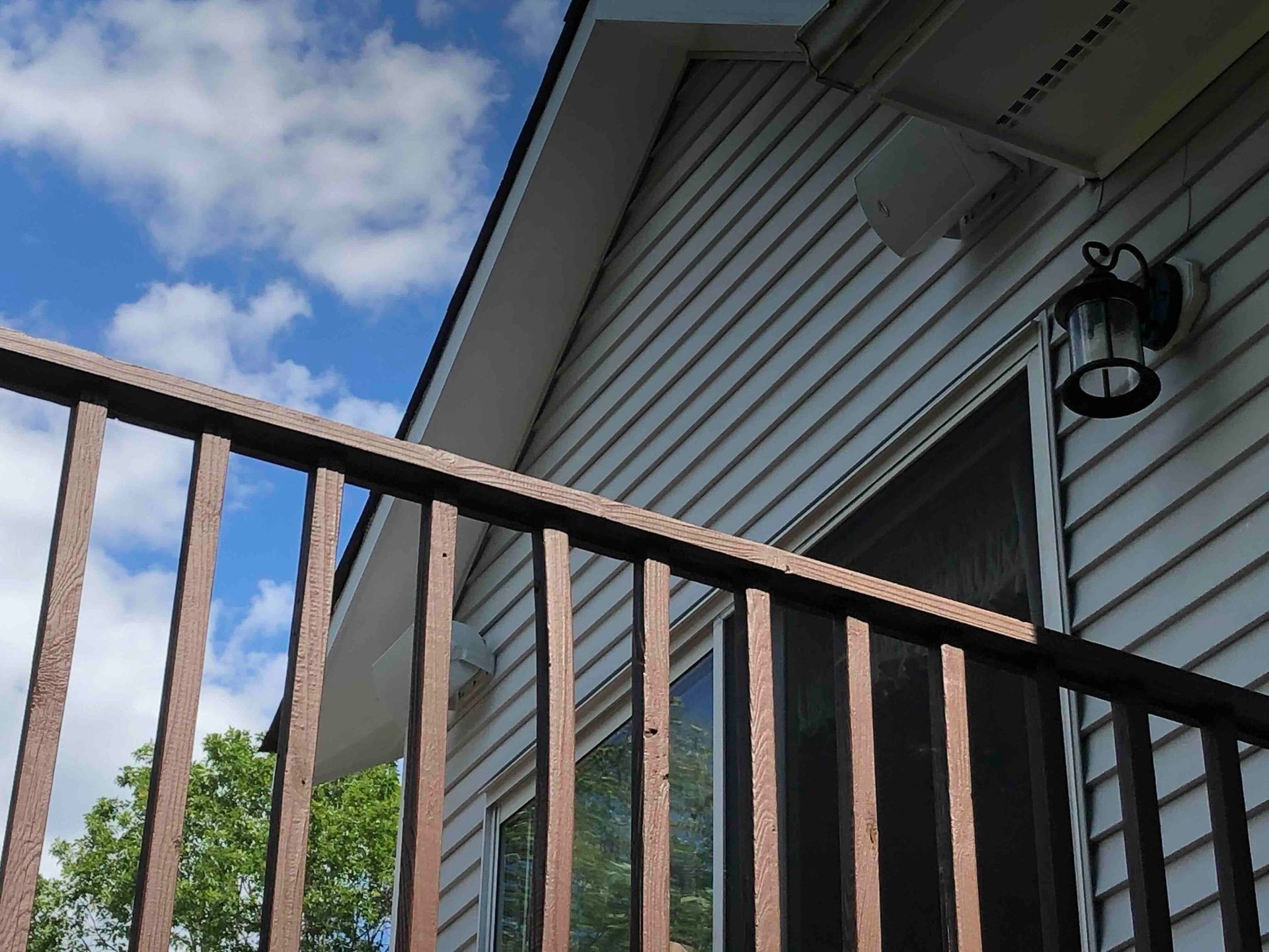 a white house with a brown railing and a lantern and a newly installed outdoor speaker