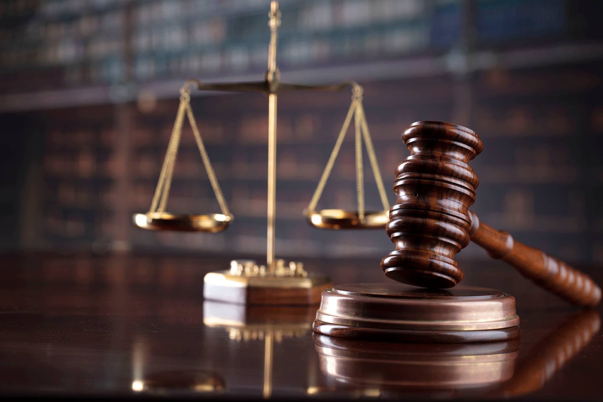 Scales of justice and wooden gavel on a table. Law books in the background.