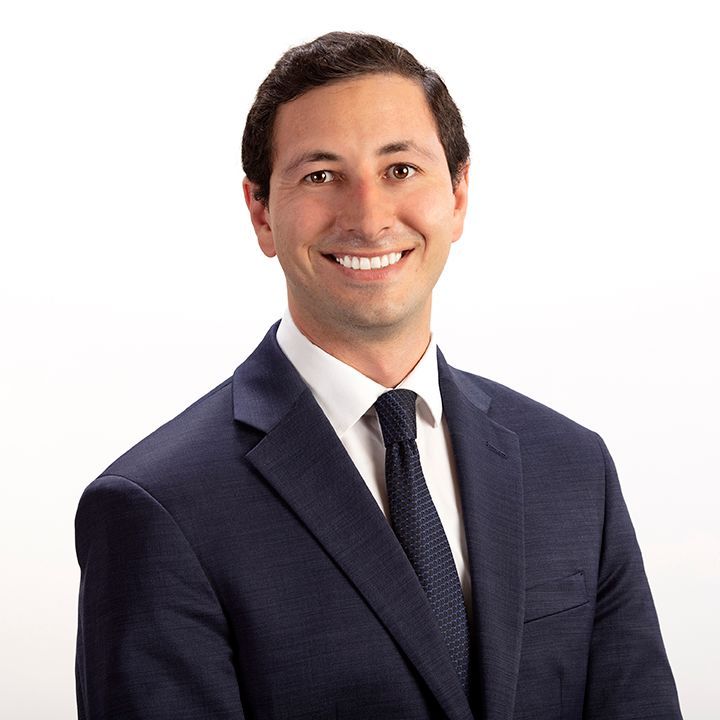 Man in navy suit and tie, smiling, posed against a white backdrop.