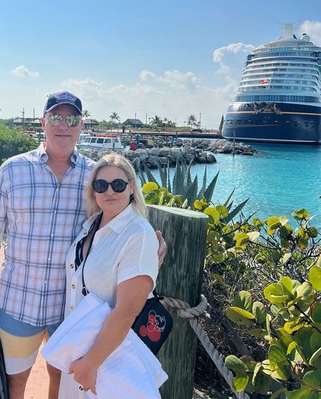 A man and a woman are posing for a picture in front of a cruise ship.