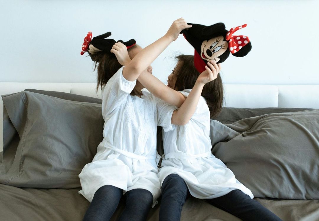 Two girls are playing with stuffed minnie mouse dolls on a bed