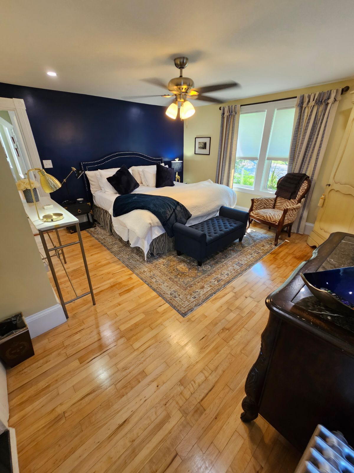Spacious bedroom with a dark blue accent wall, hardwood floors, and a queen-sized bed.