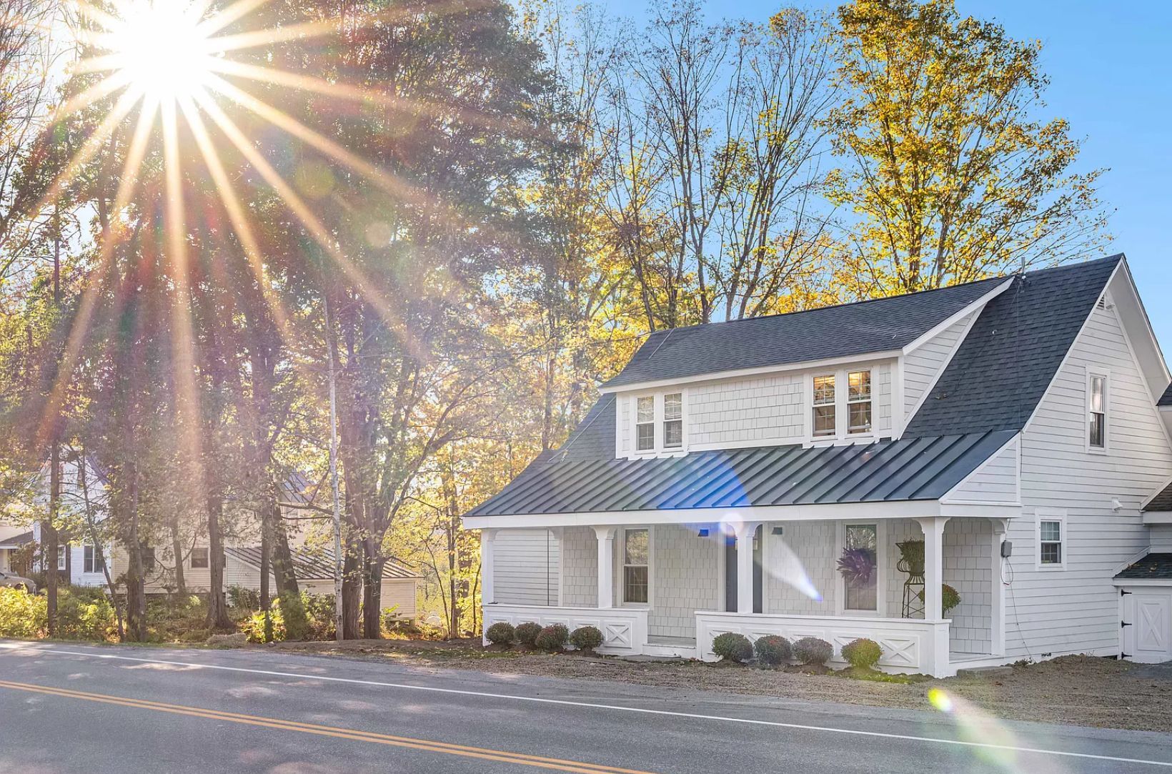 White house with a dark roof and porch under a bright sun.