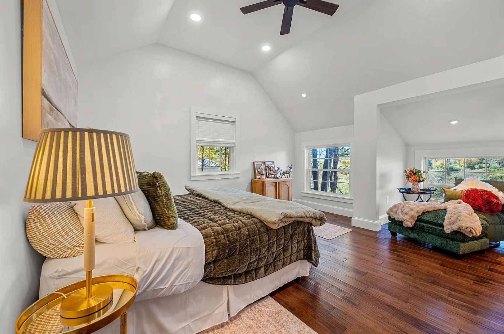 Bedroom with vaulted ceiling, bed, seating area, and hardwood floor.