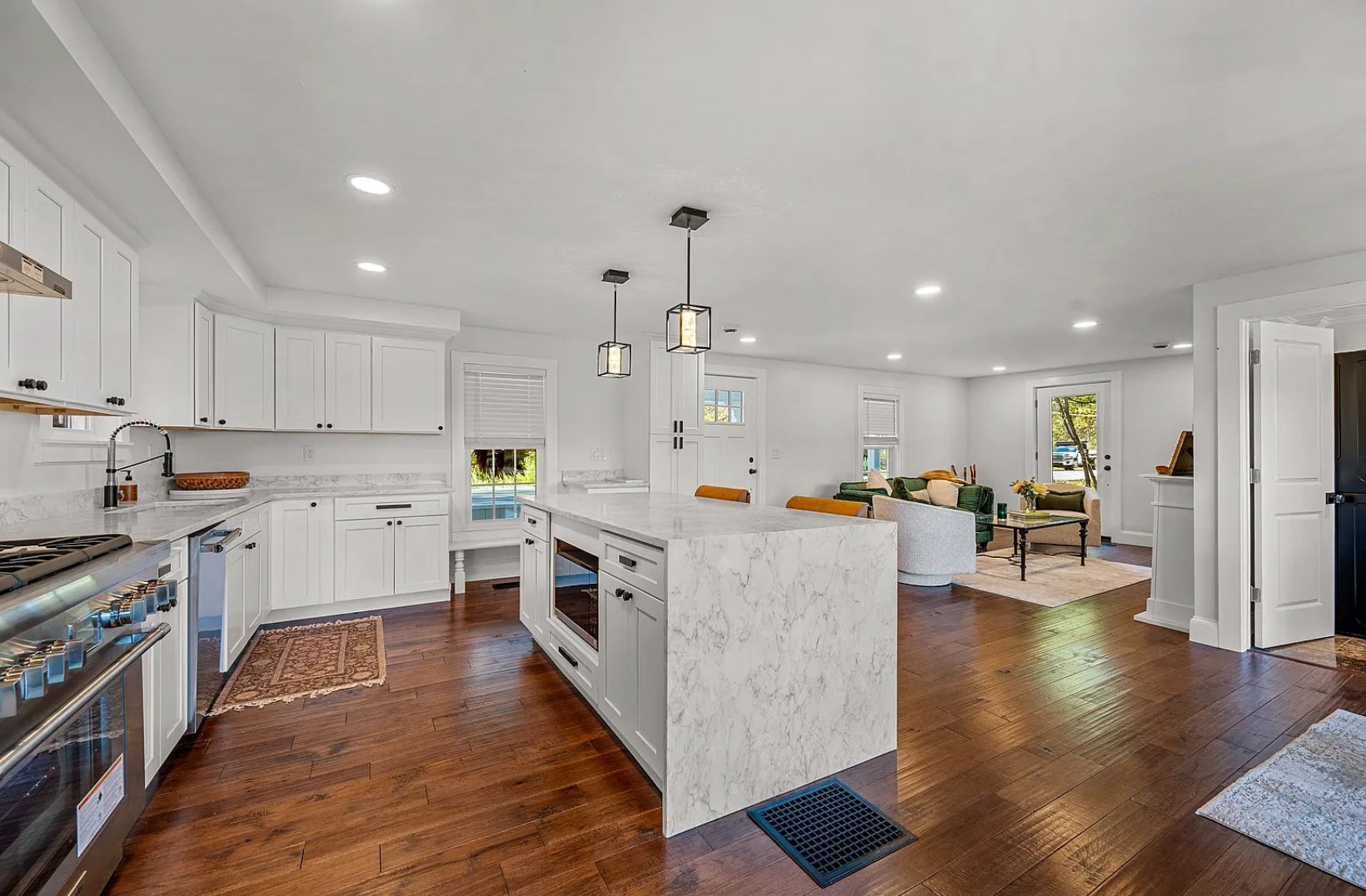 Open-concept kitchen and living room with white cabinets, marble island, and dark wood floors.