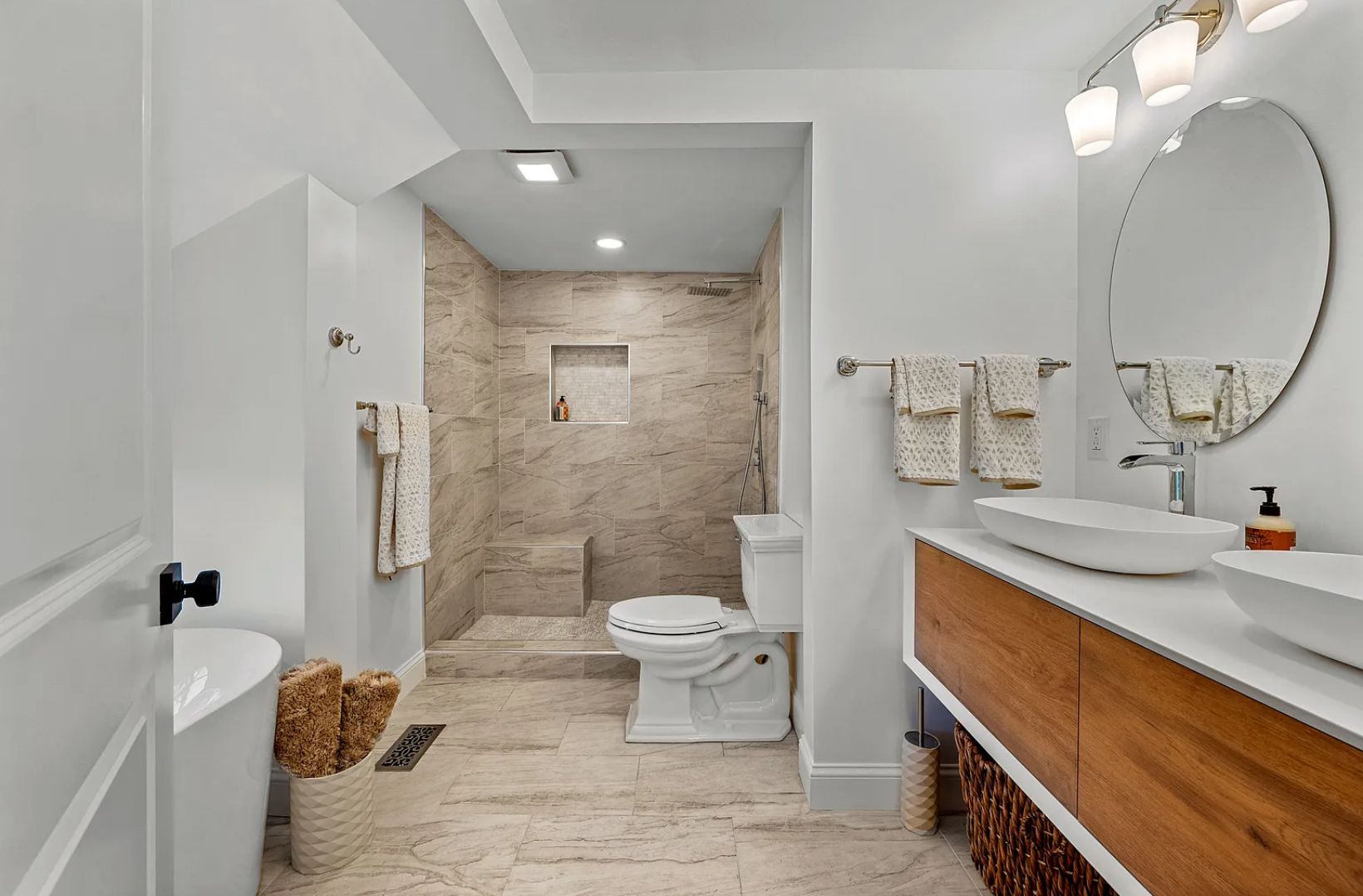 Modern bathroom with walk-in shower, toilet, double vanity with oval mirror, and a standalone tub.