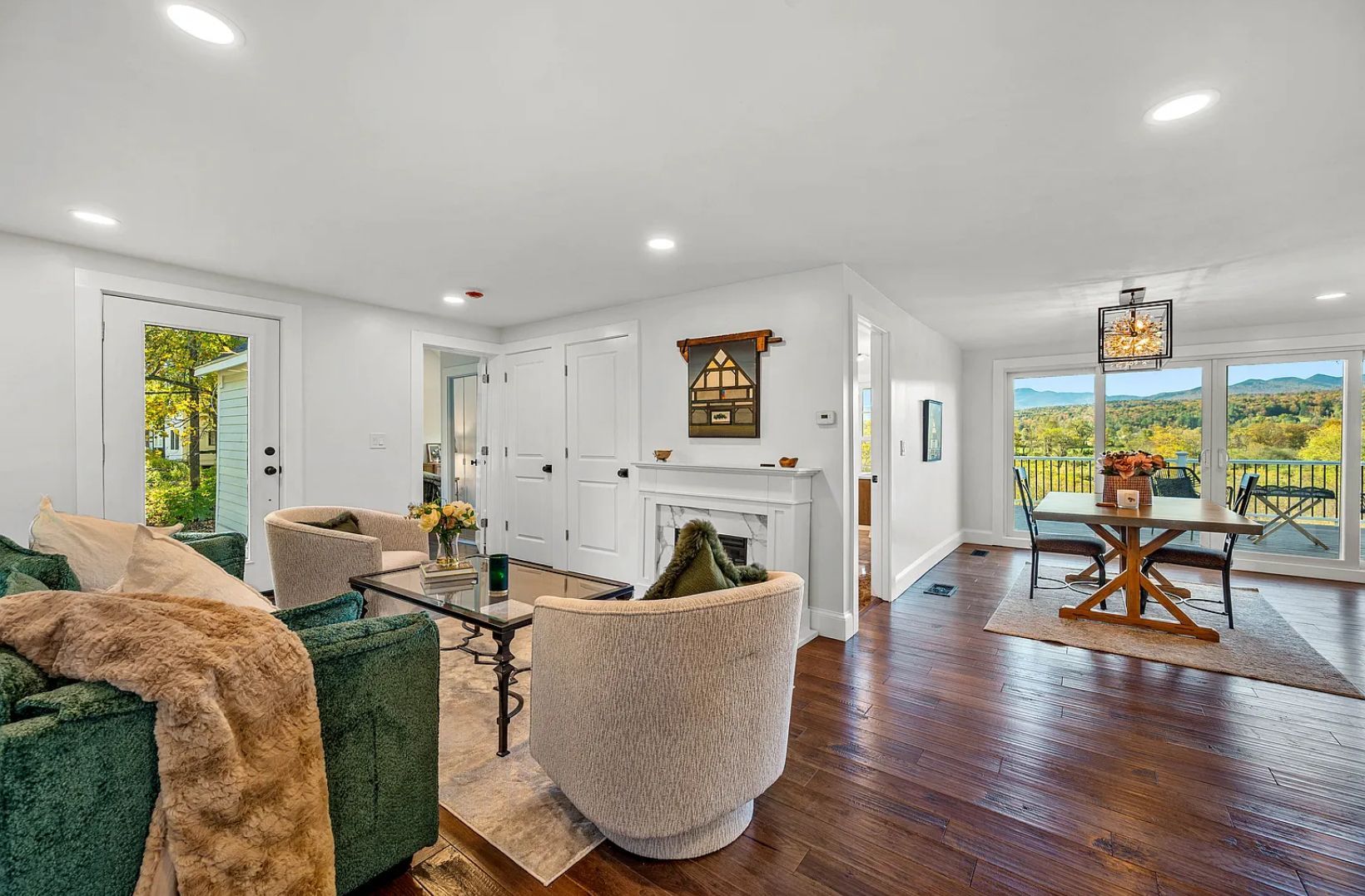 Living room with green sofa, cream chairs, dark wood floors, and view of a table on a deck.