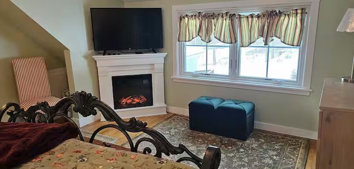 Cozy living room with fireplace, wall-mounted TV, window seat, and blue ottoman