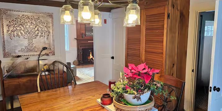 Dining room with wooden table, hanging lights, and pink flowers on a centerpiece near louvered doors.