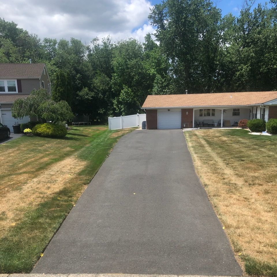 A driveway leading to a house with a white fence.