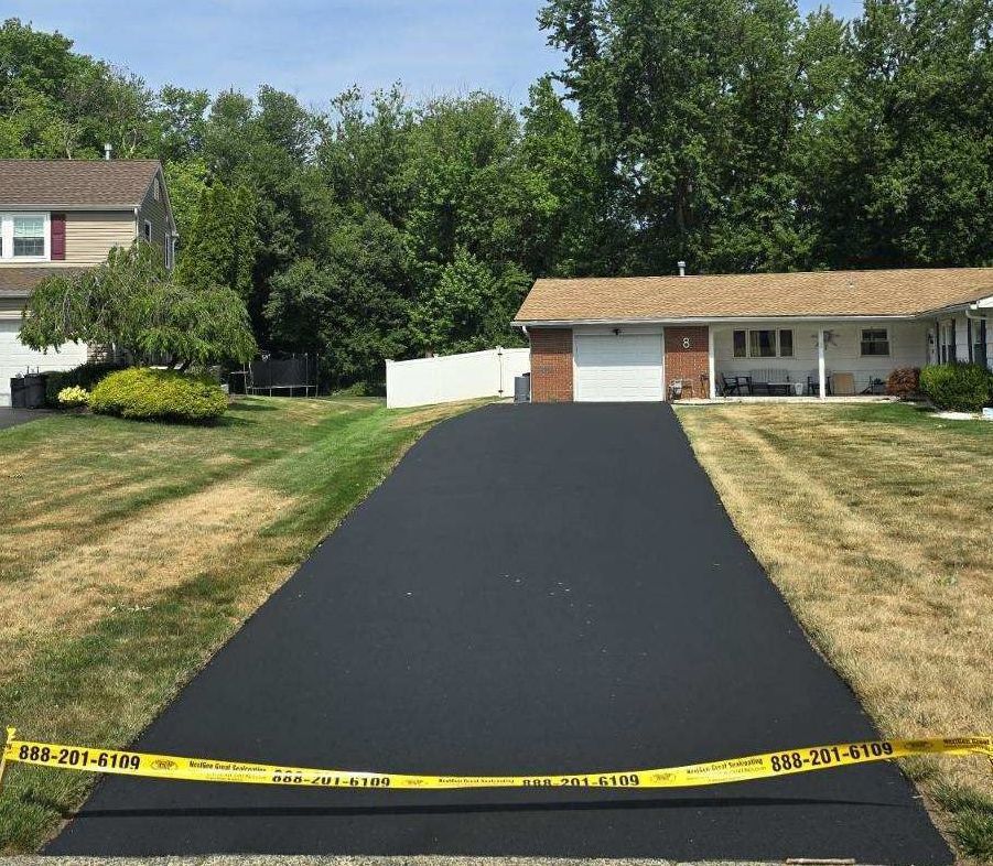 A black driveway leading to a house with a white fence.