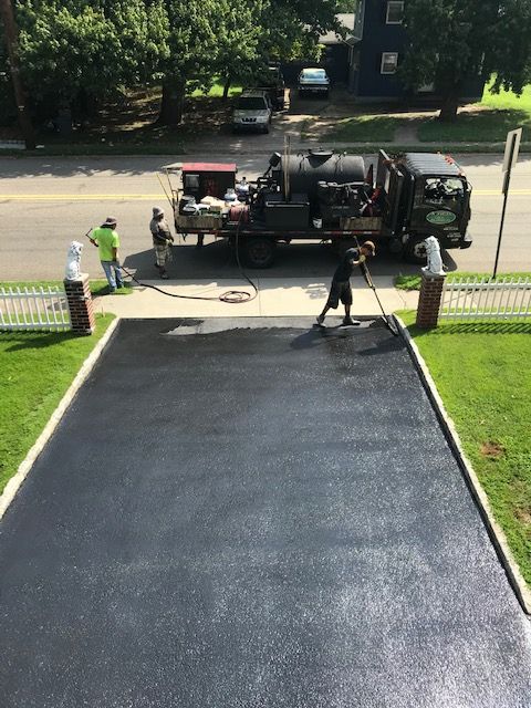 A man is painting a driveway with a truck in the background.