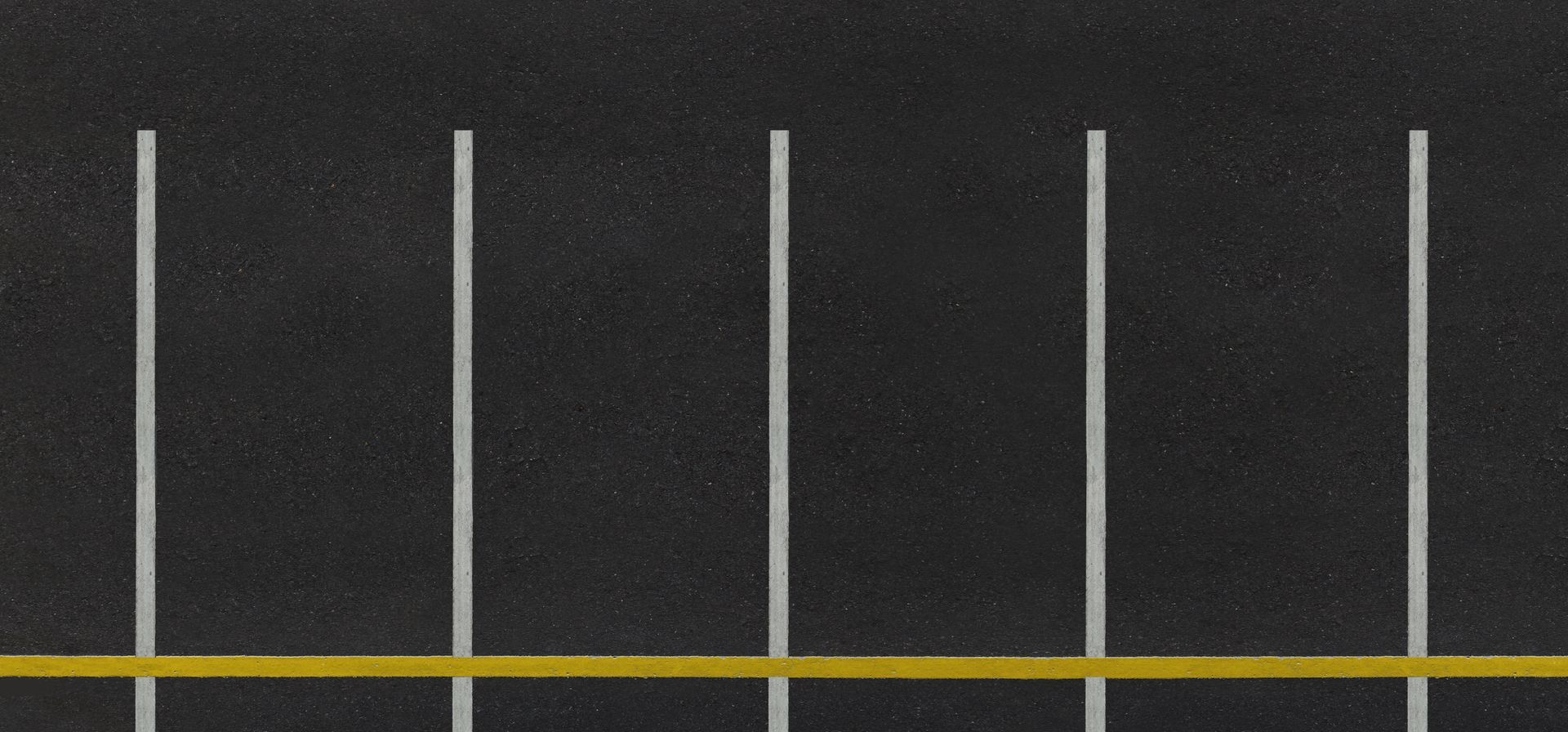 Empty parking lot with white stall lines and a yellow curb stripe on dark pavement