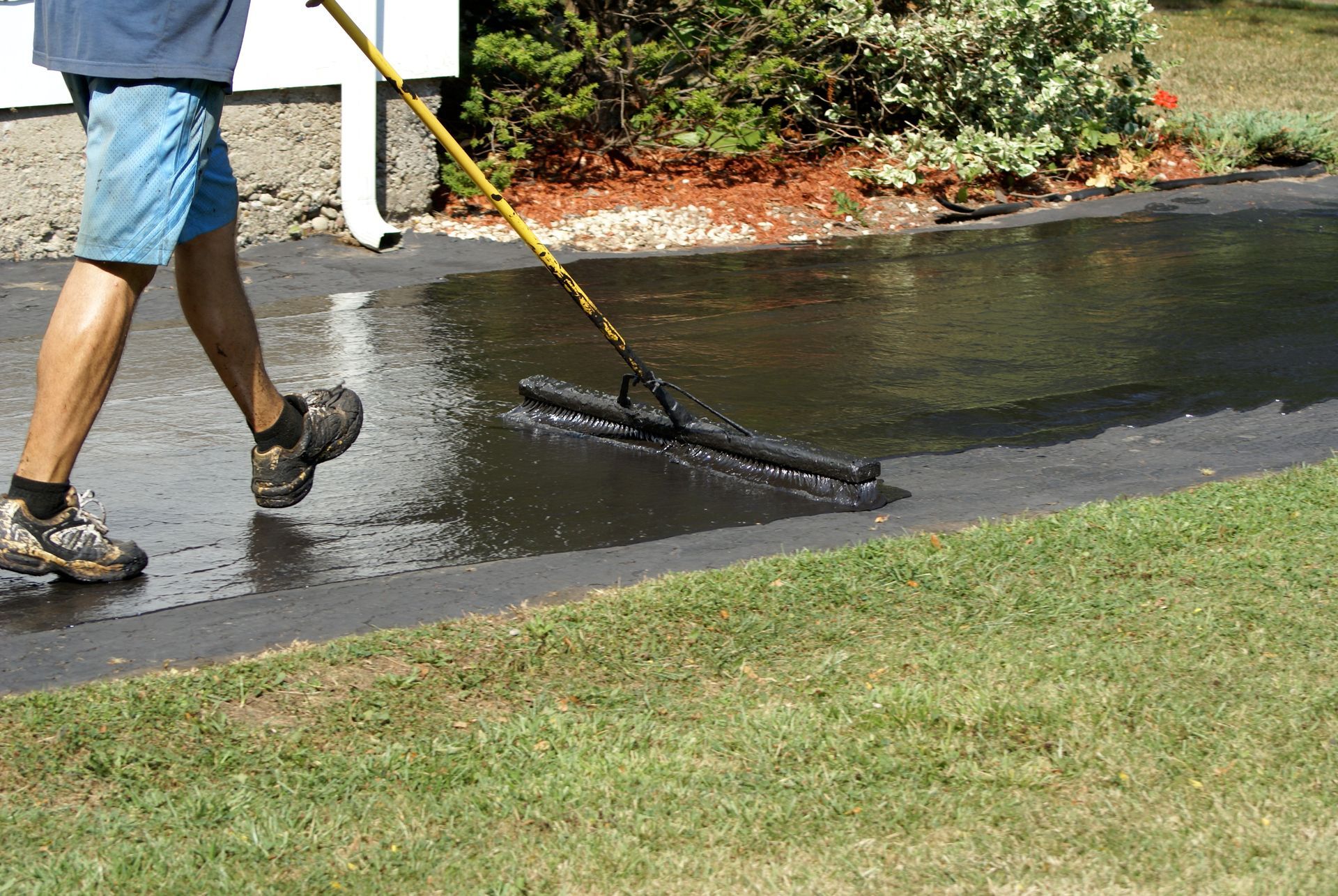 A person using a squeegee to spread black asphalt sealant across a residential driveway.