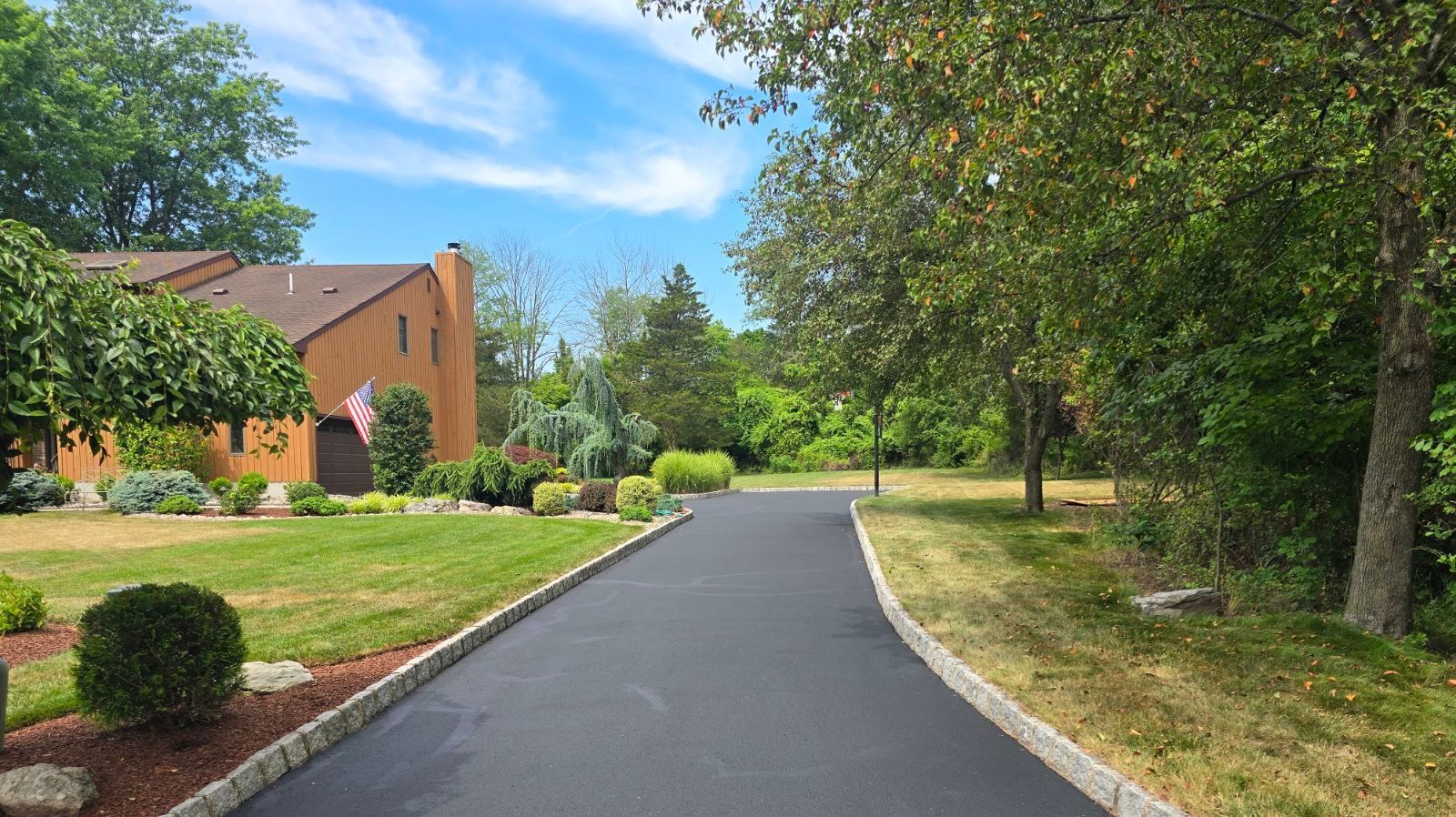 A black driveway leading to a house with a white fence.