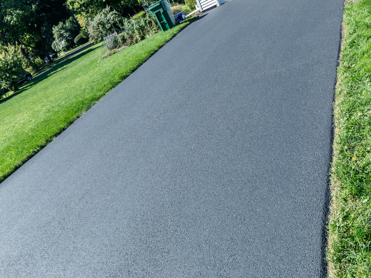 A black asphalt driveway surrounded by grass and trees.