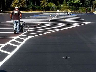 A man is walking down a parking lot with a hose.