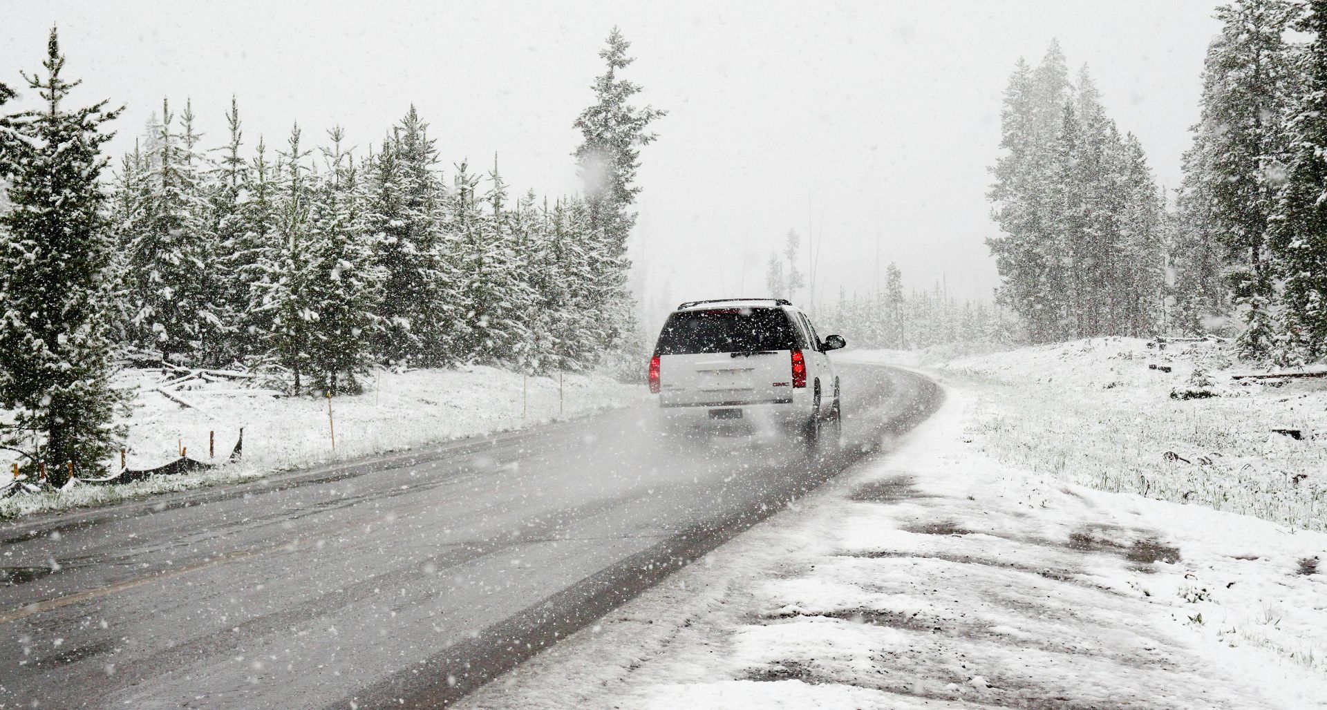 A white suv is driving down a snowy road.