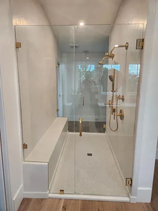 A bathroom with a glass shower door and a bench.