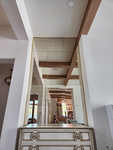 A large mirror is hanging from the ceiling above a dresser in a living room.