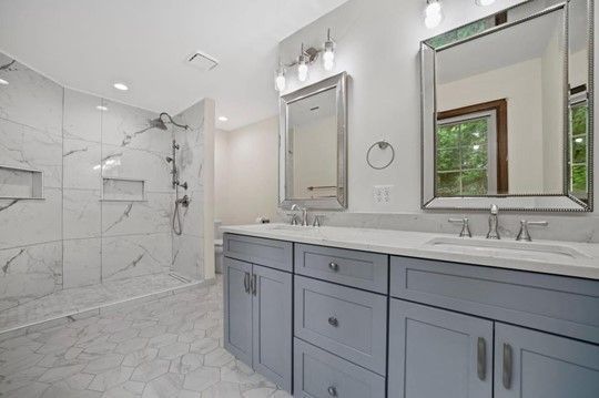 A bathroom with two sinks , two mirrors and a walk in shower.