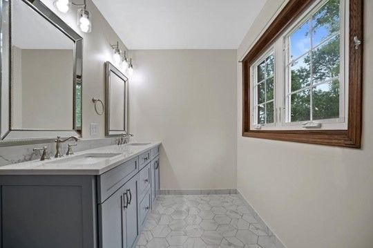 A bathroom with two sinks , two mirrors and two windows.