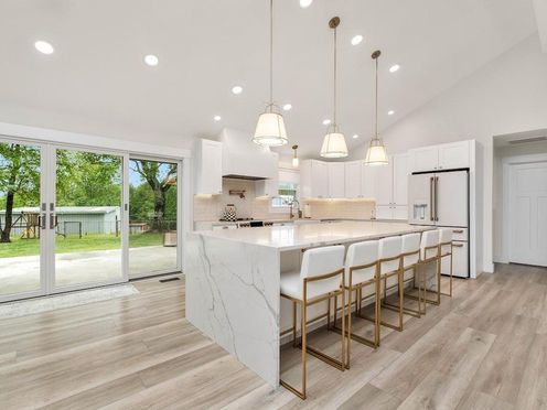 A kitchen with a large island , stools , and a refrigerator.