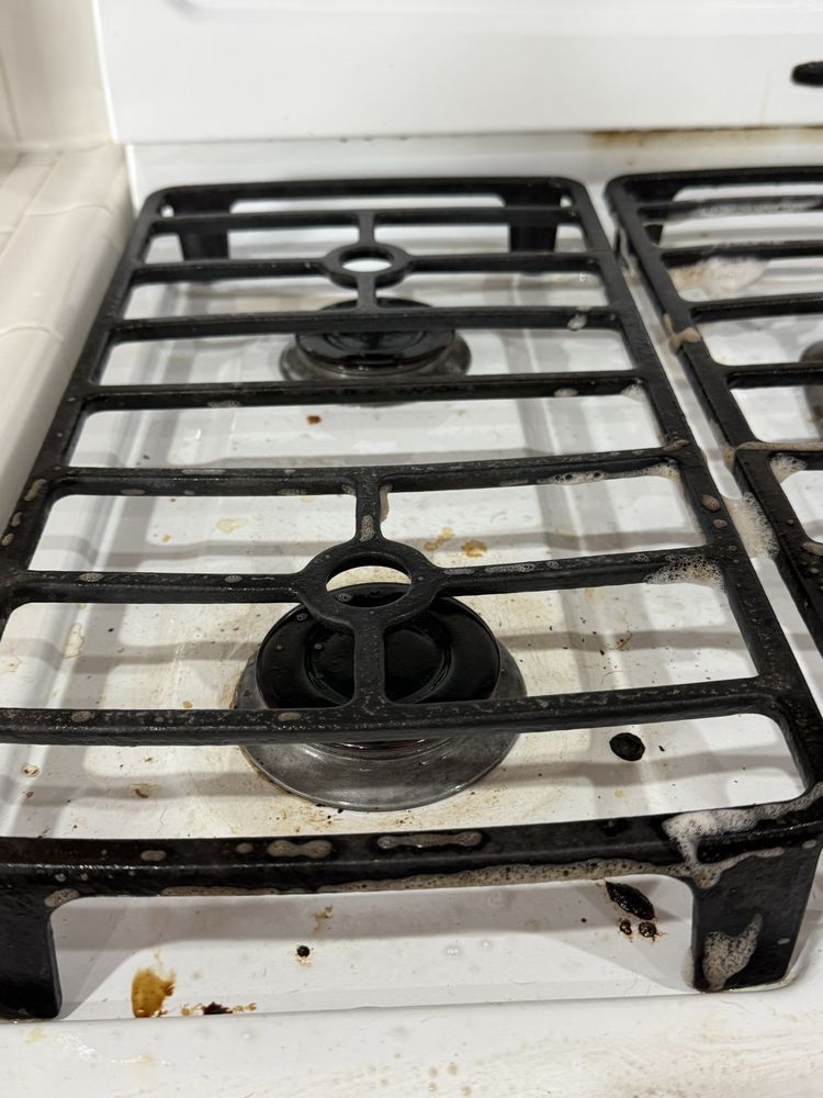 Dirty black gas stove burners on a white stovetop with grease stains and crumbs