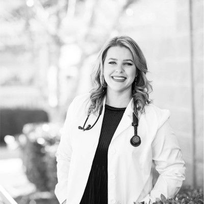 A woman in a lab coat with a stethoscope around her neck is smiling in a black and white photo.
