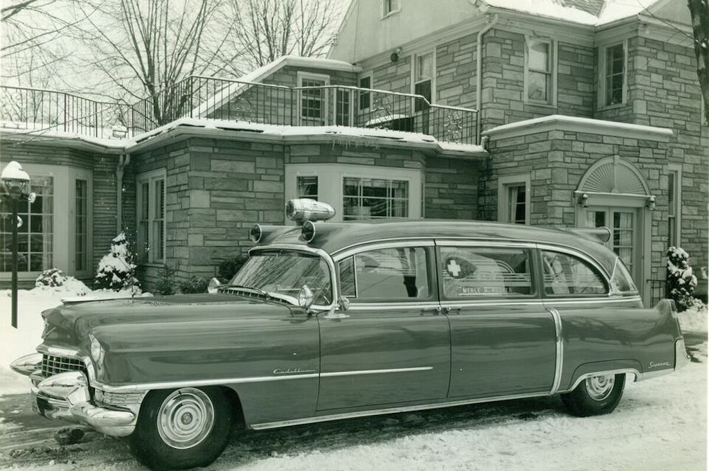 A black and white photo of an ambulance parked in front of a stone building