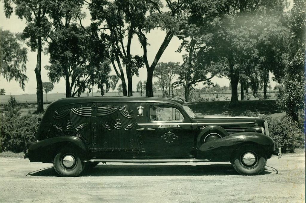 A black and white photo of a limousine parked in front of trees