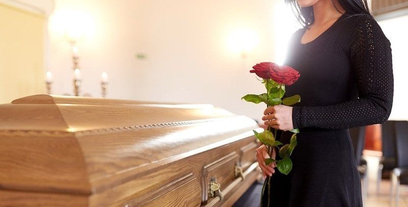 a woman is holding a red rose in front of a coffin .