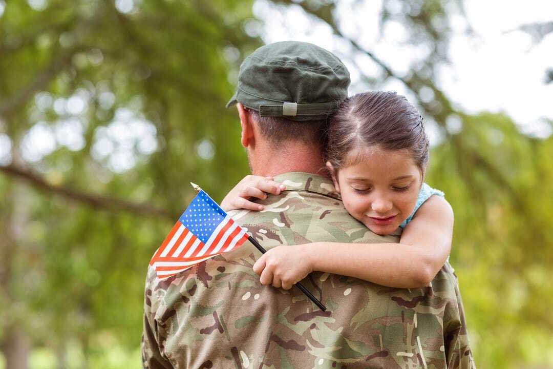 a little girl hugging a soldier with an american flag on his back