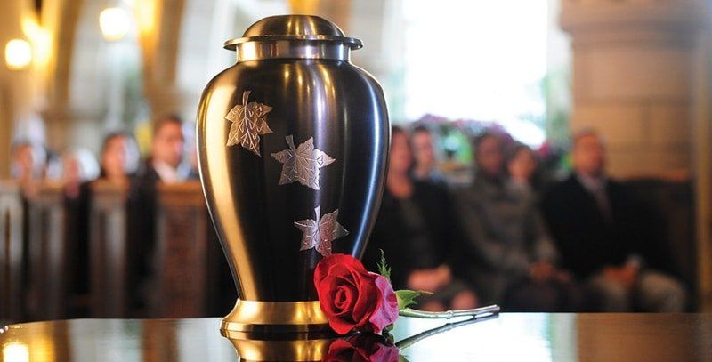 a black urn with silver leaves sits on a table next to a red rose