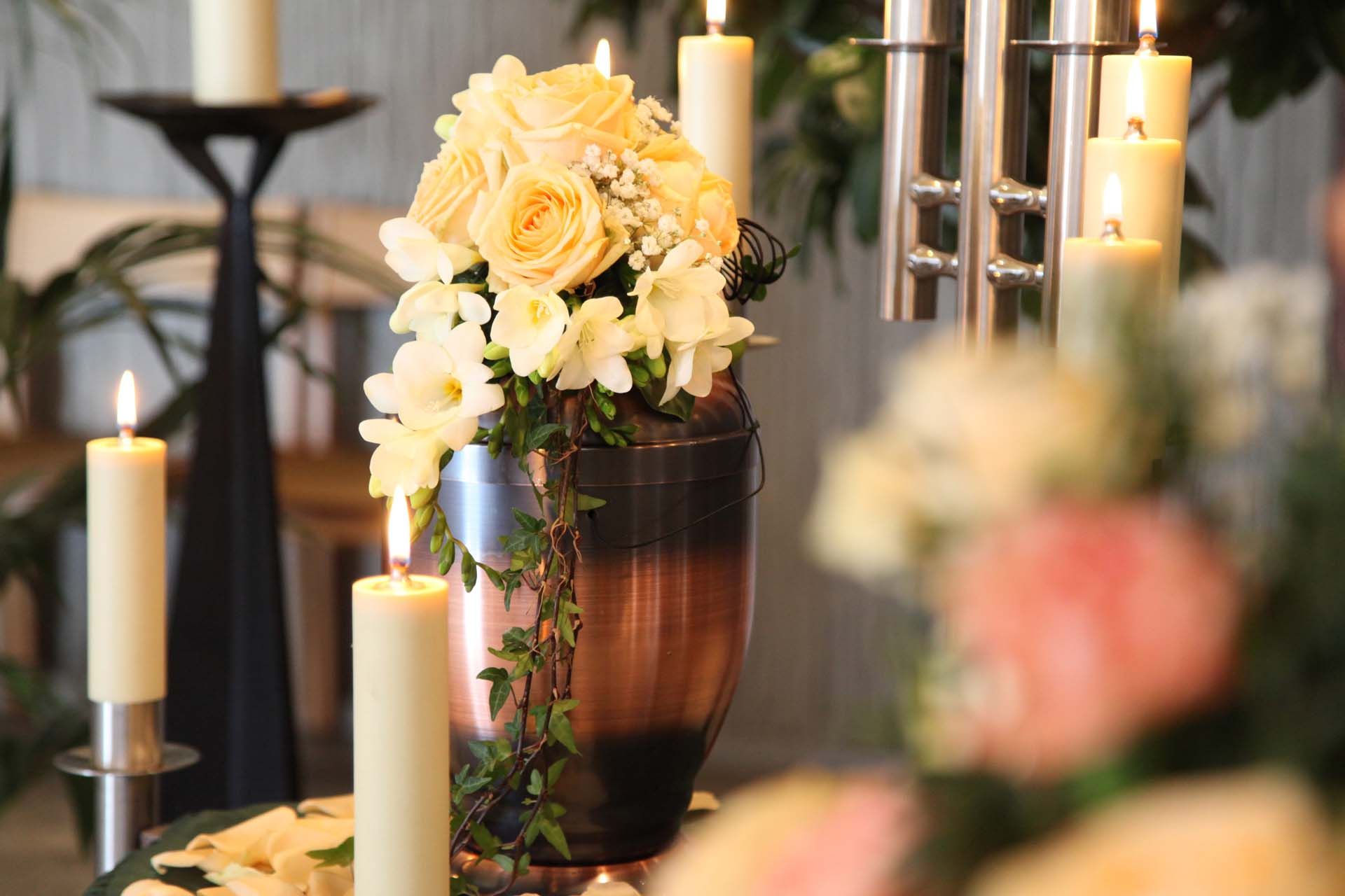 a black urn with silver leaves sits on a table next to a red rose