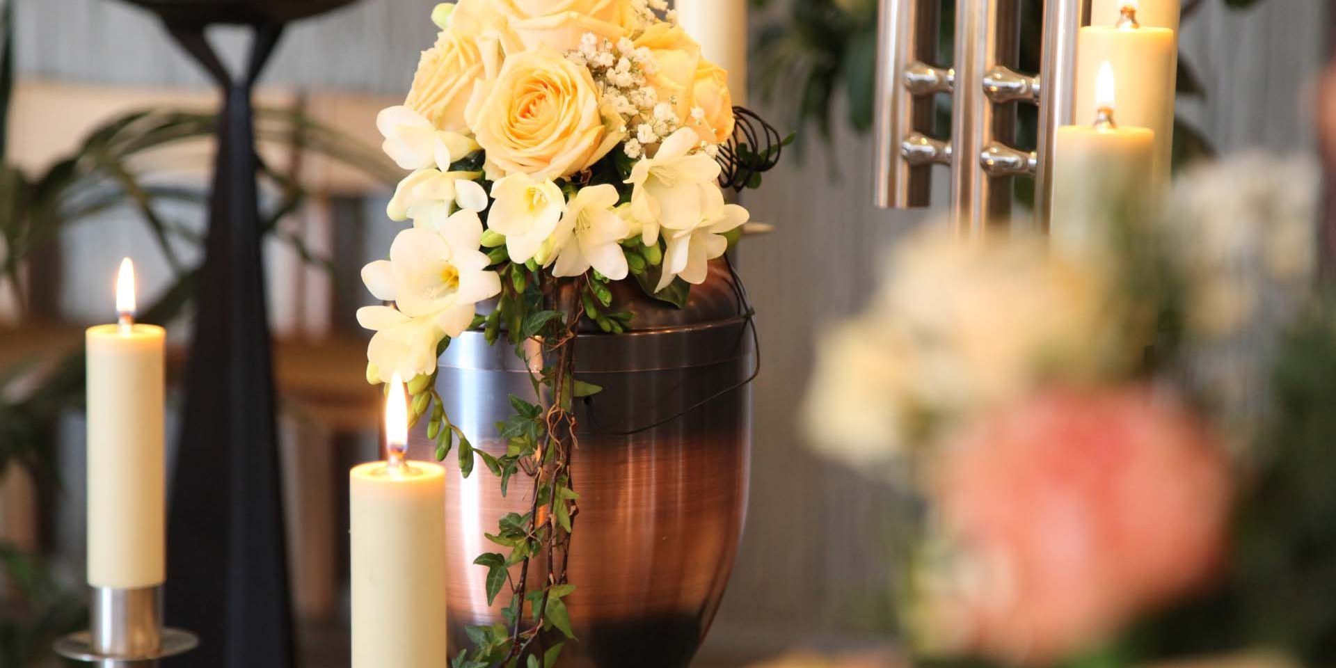 a black urn with leaves on it sits on a table next to a red rose