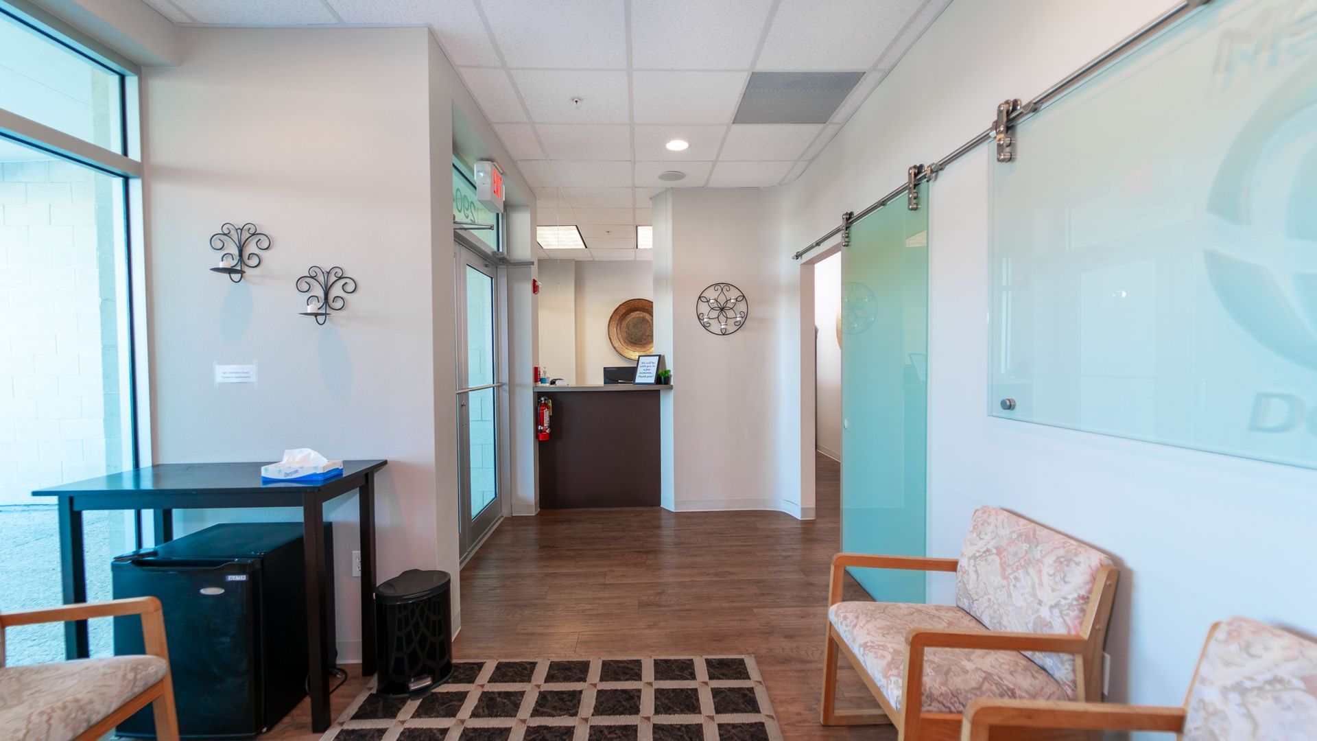 A waiting room with chairs , a table and a sliding glass door.